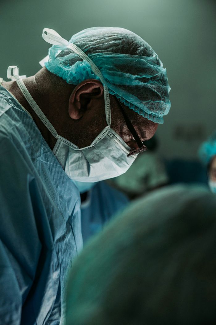 A surgeon in scrubs and a mask performs surgery in a sterile hospital operating room, focused on the patient.